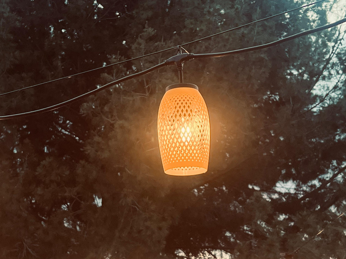 Yellow lattice-weave lantern cover glowing softly at dusk among trees — Groovy Lanterns