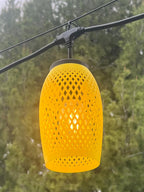 Yellow lattice-weave lantern cover glowing over string lights among trees — Groovy Lanterns