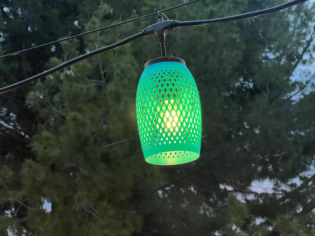 Green lattice-weave lantern cover glowing at dusk among trees — Groovy Lanterns