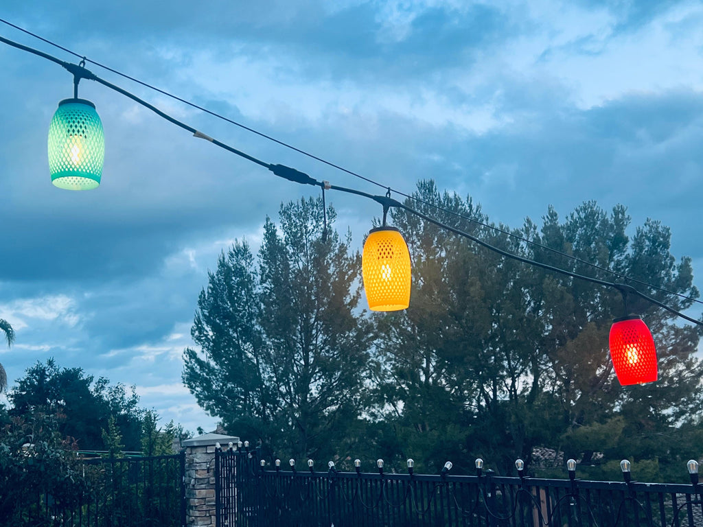 Green, yellow, and red lattice lantern covers glowing along a string at dusk — Groovy Lanterns