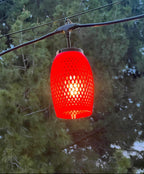 Red lattice-weave lantern cover glowing at dusk among trees — Groovy Lanterns