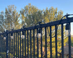 String of drop-style fence clips holding lit bulbs along a fence rail at golden hour — Groovy Lanterns