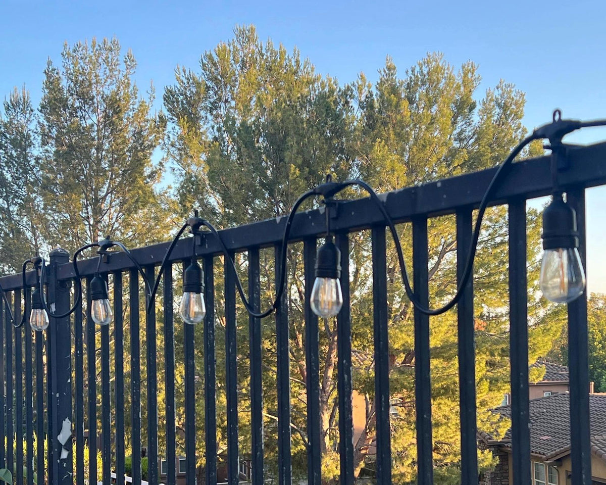 String of drop-style fence clips holding lit bulbs along a fence rail at golden hour — Groovy Lanterns