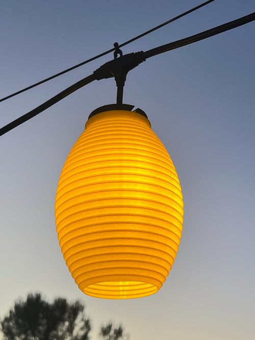 The Frolic lantern cover glowing amber over string lights at dusk — Groovy Lanterns