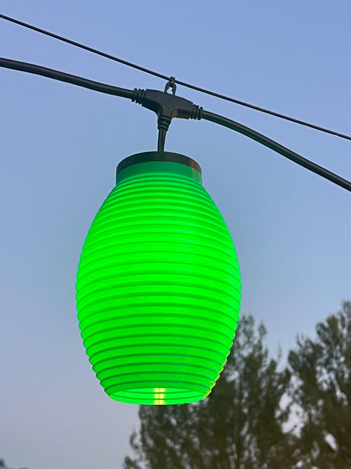 The Frolic lantern cover glowing green over string lights at dusk — Groovy Lanterns